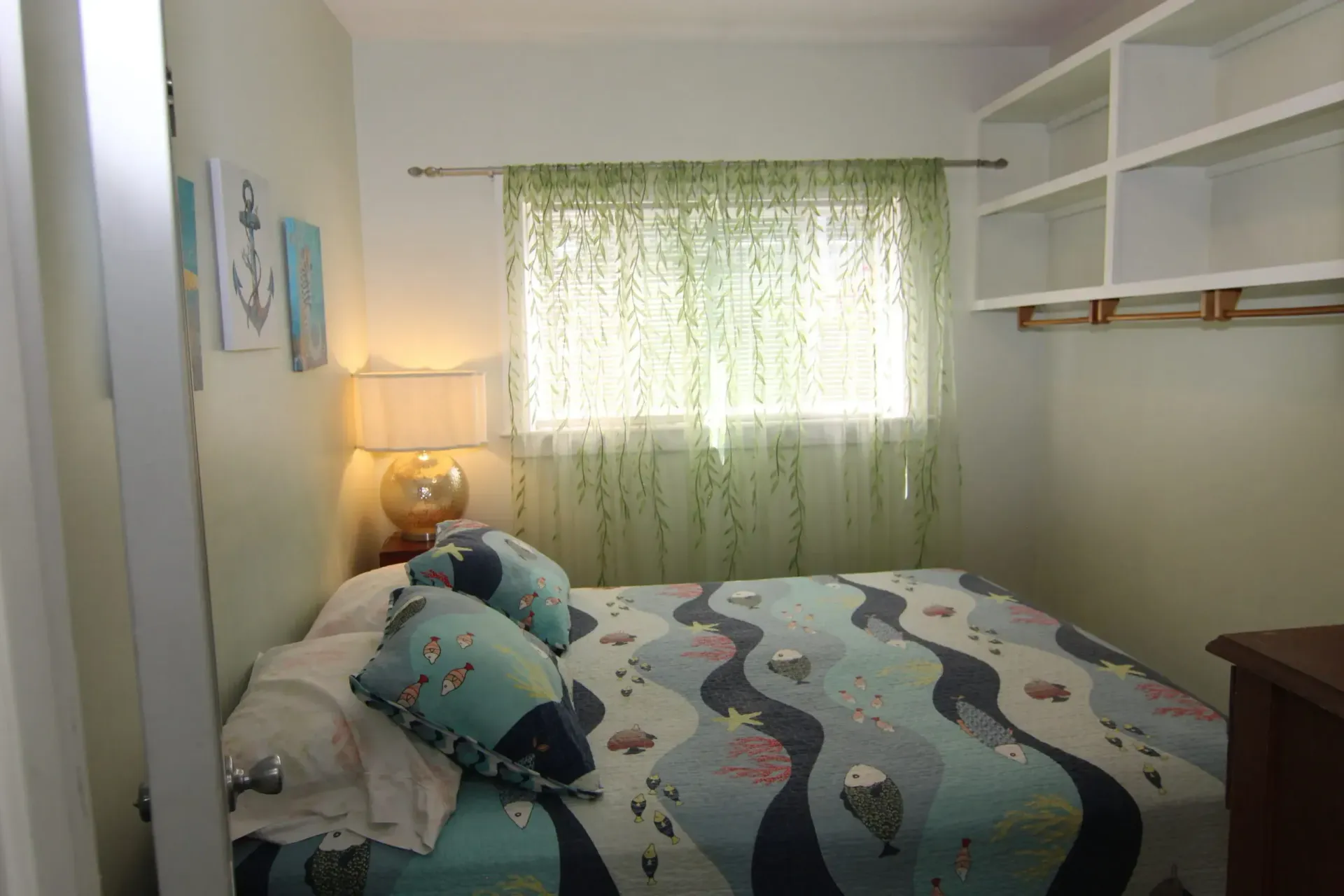 Bedroom with bed, window, built-in shelves, and artwork. 