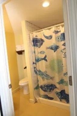 Bathroom with a toilet, shower with fish-patterned curtain, and yellow walls, viewed from doorway.