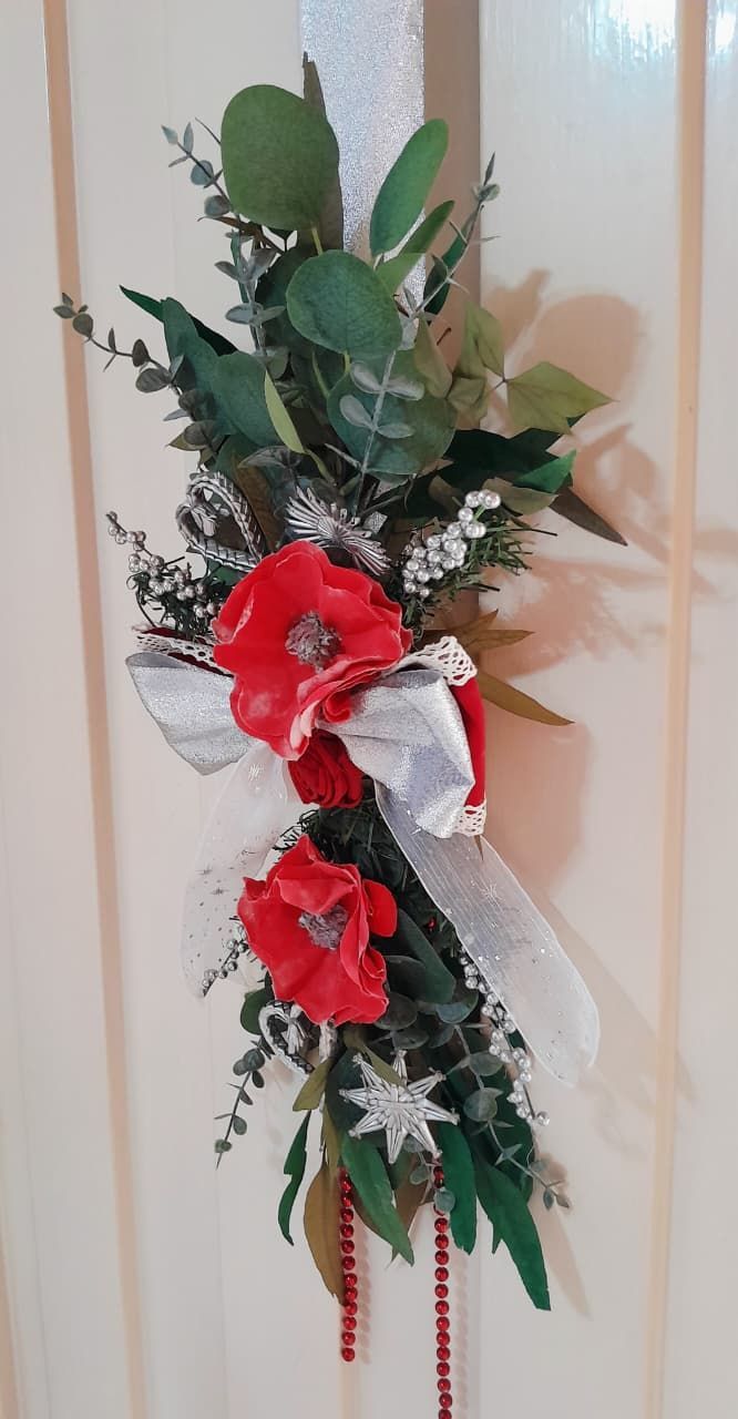 Arreglo floral con flores rojas, cinta plateada y vegetación sobre fondo blanco.