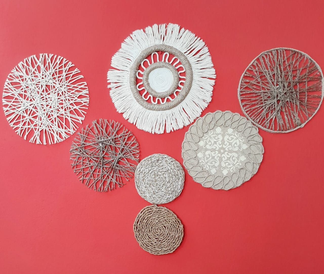 Siete tapices decorativos redondos en tonos beige y blanco sobre una pared roja.