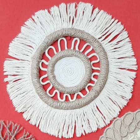 Colgante de pared de macramé blanco y tostado sobre fondo rojo.