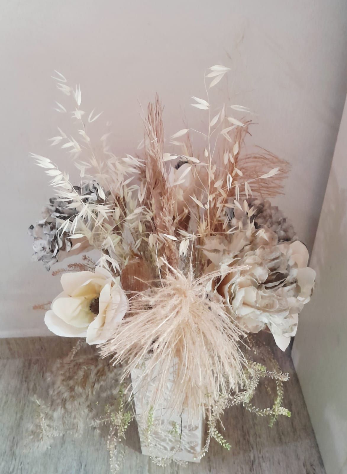 Arreglo de flores secas en un jarrón de textura transparente, con tonos neutros de crema, bronceado y marrón.