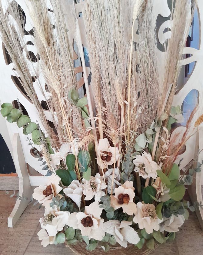 Arreglo floral con pasto de pampa, flores blancas y vegetación en un recipiente de madera decorativo y calado.