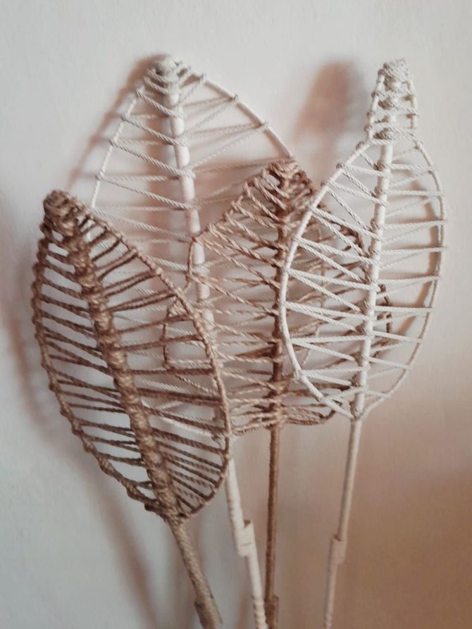 Cuatro esculturas de hojas con estructura de alambre de distintos tamaños, blancas y marrones, sobre una pared blanca.