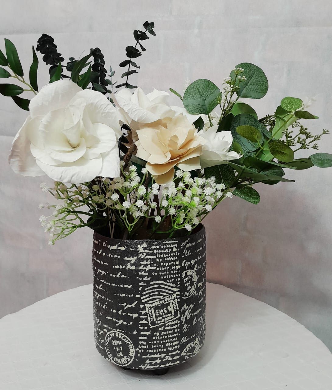 Arreglo floral en jarrón con estampado negro, con flores de color blanco y crema con follaje verde.