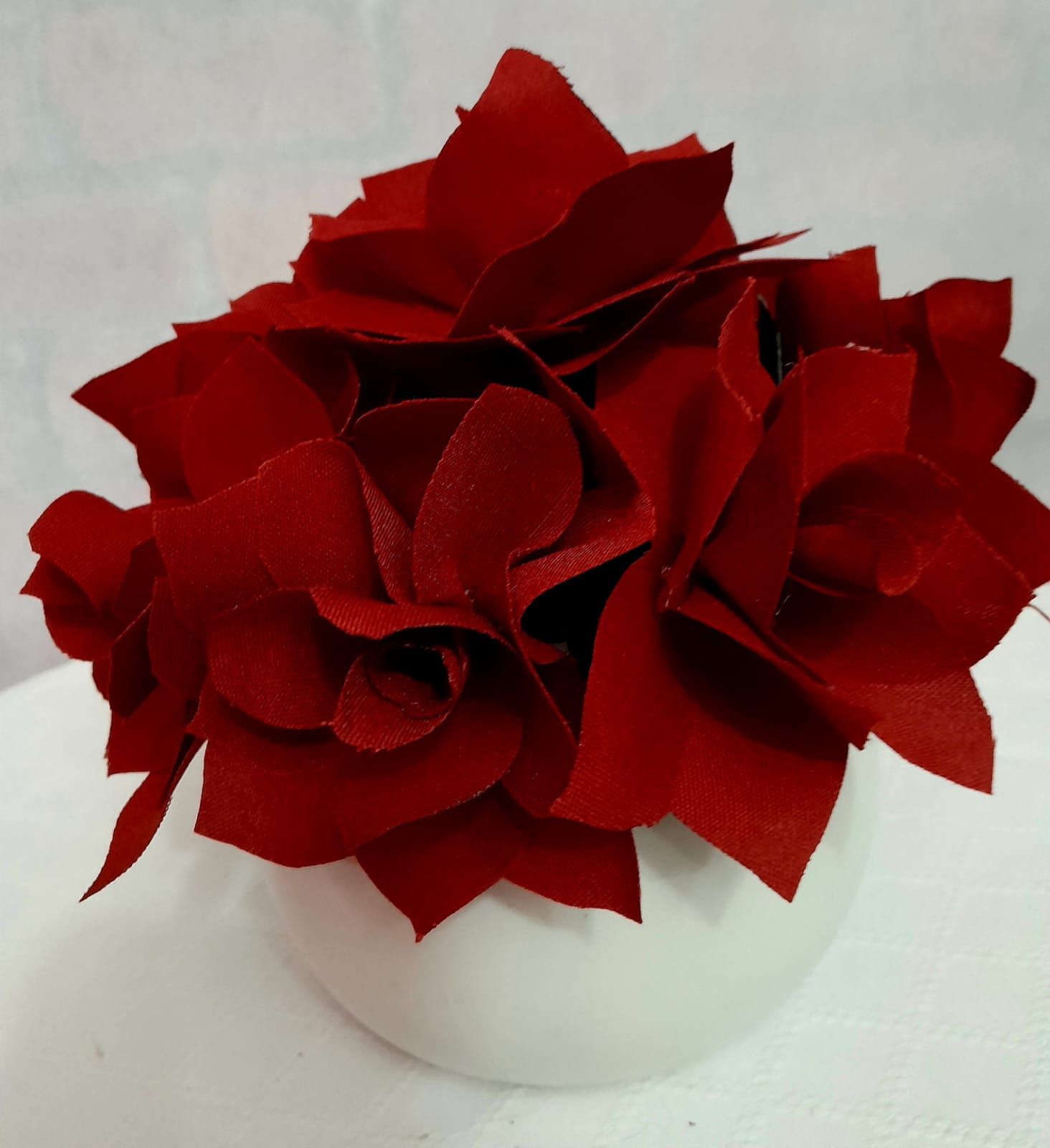 Flores de tela roja en jarrón blanco y redondo.