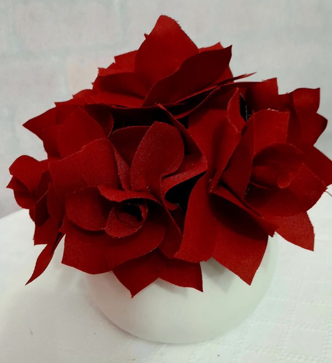 Flores de tela roja en jarrón blanco y redondo.