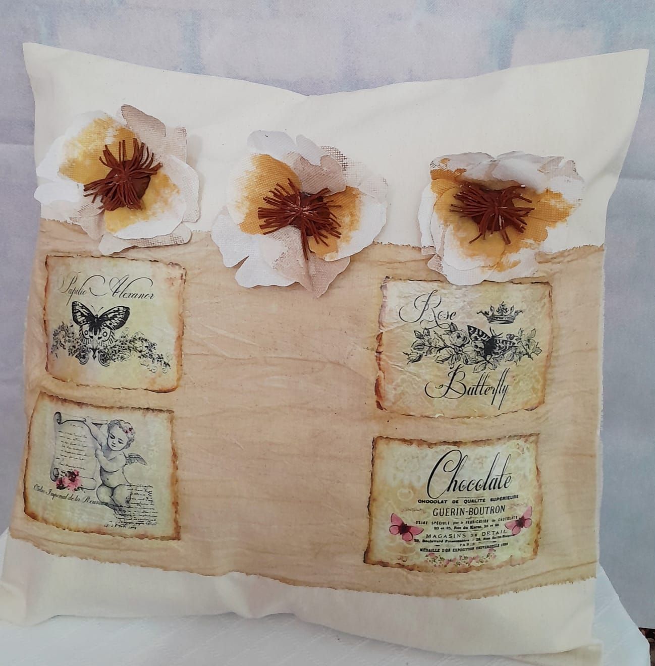 Almohada de color crema con flores de tela, estampados vintage y una raya color tostado.