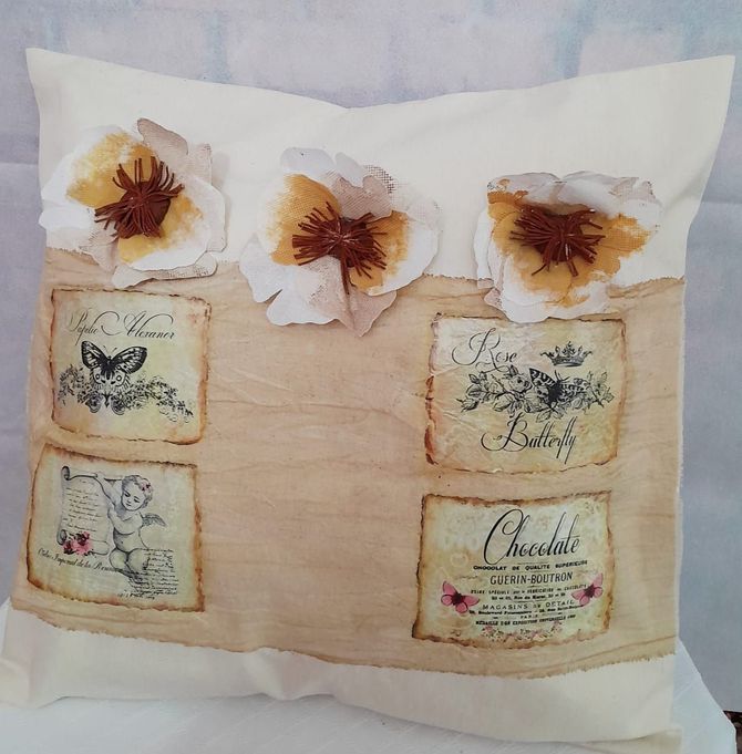 Almohada de color crema con flores de tela, estampados vintage y una raya color tostado.