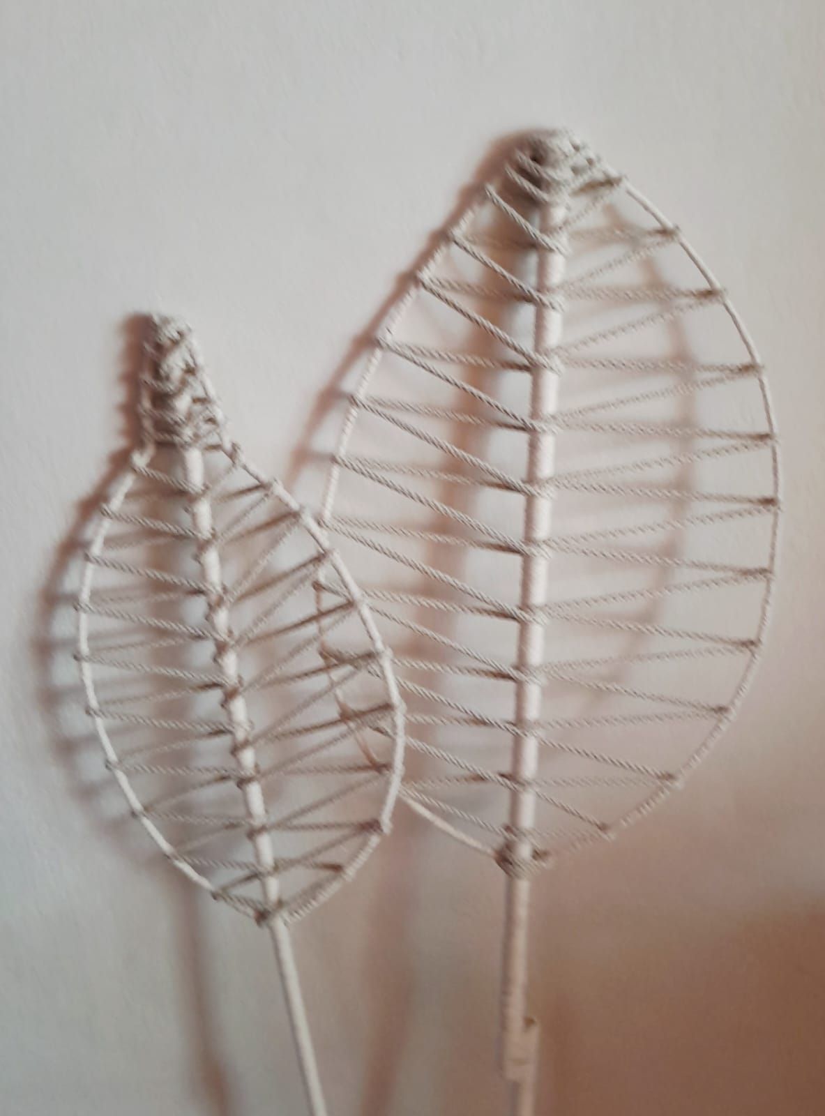 Dos esculturas de alambre blancas, con forma de hojas, contra una pared lisa, proyectando sombras.
