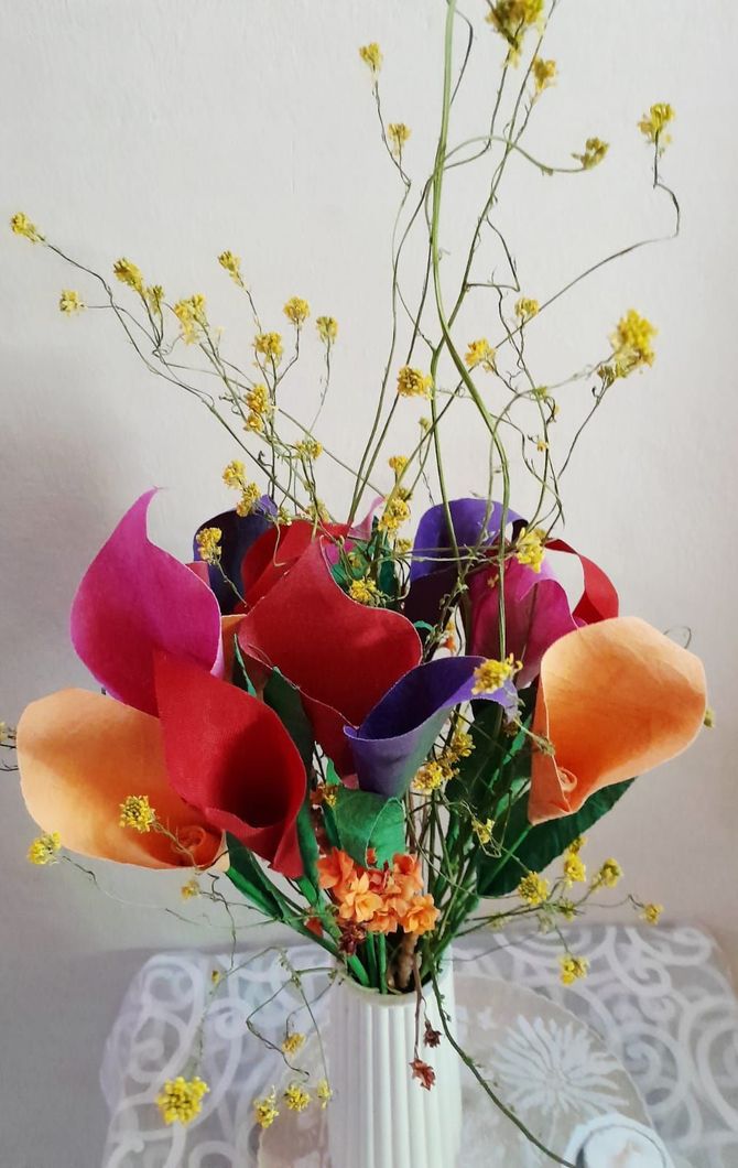 Lirios de cala coloridos en un jarrón blanco con tenues flores amarillas.