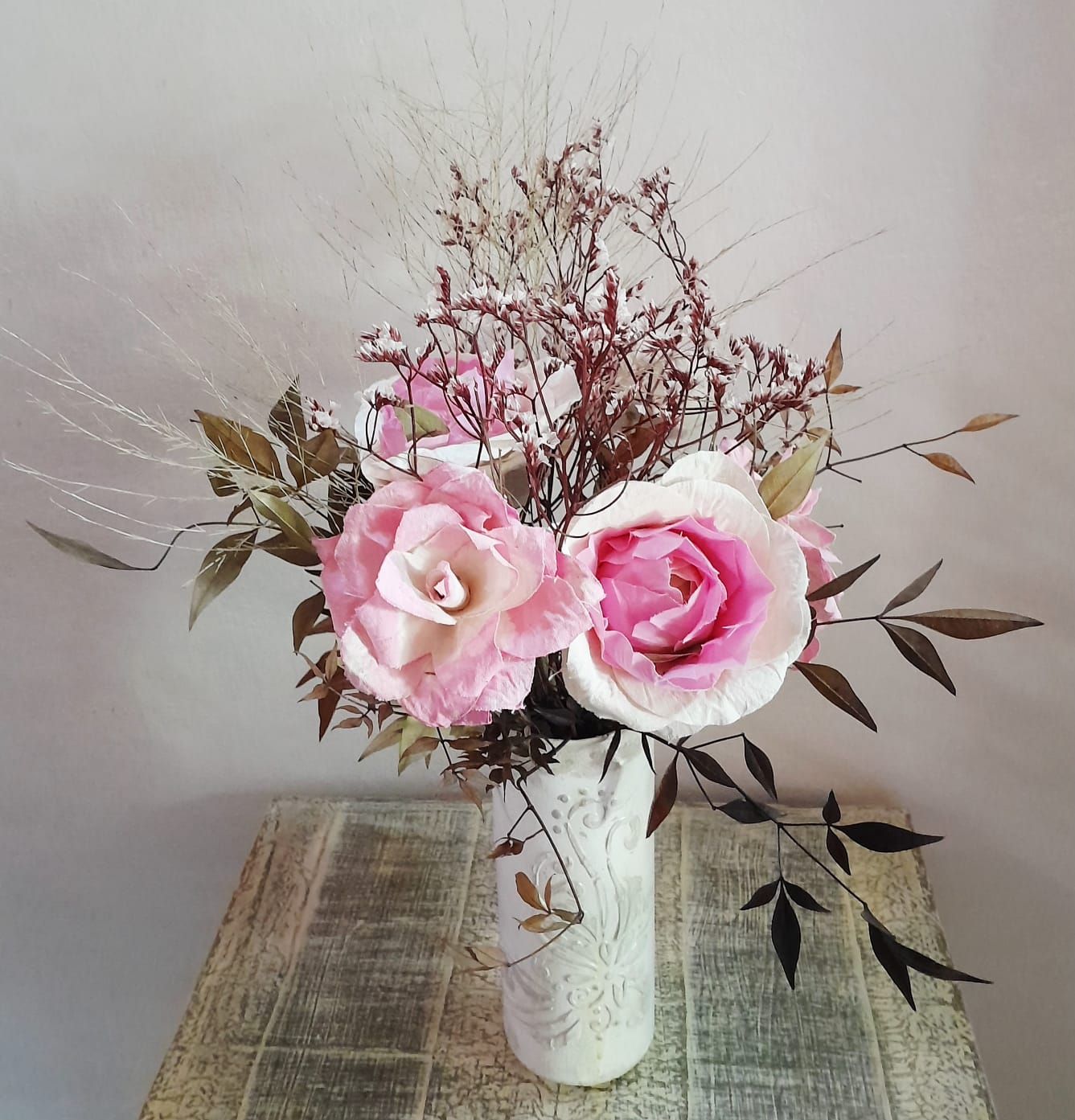 Ramo de rosas rosadas y blancas en un jarrón decorativo sobre una superficie de madera.