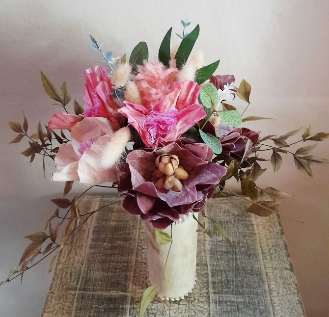 Ramo de flores rosas, moradas y verdes en un jarrón sobre una superficie de madera rústica.