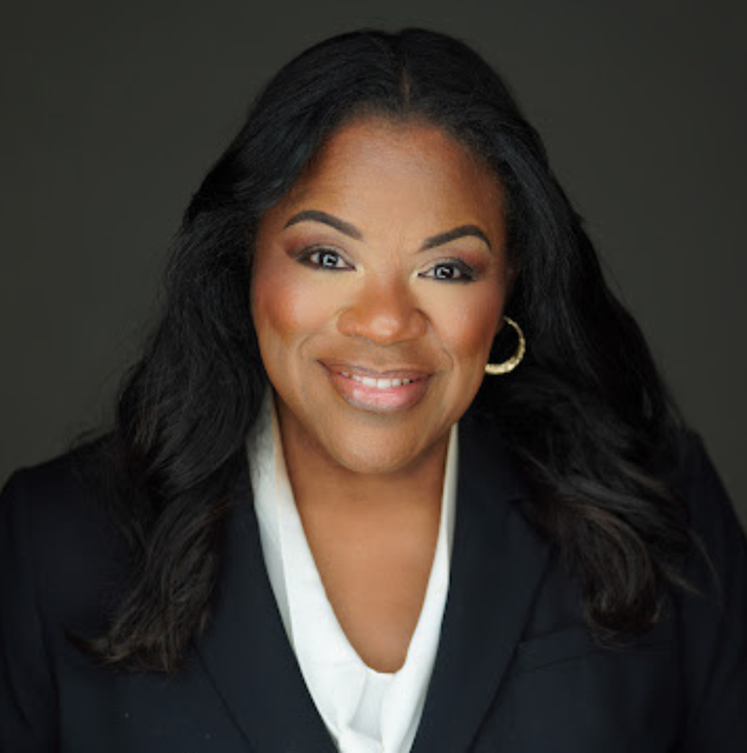 Smiling woman in a black blazer and white blouse against a dark background