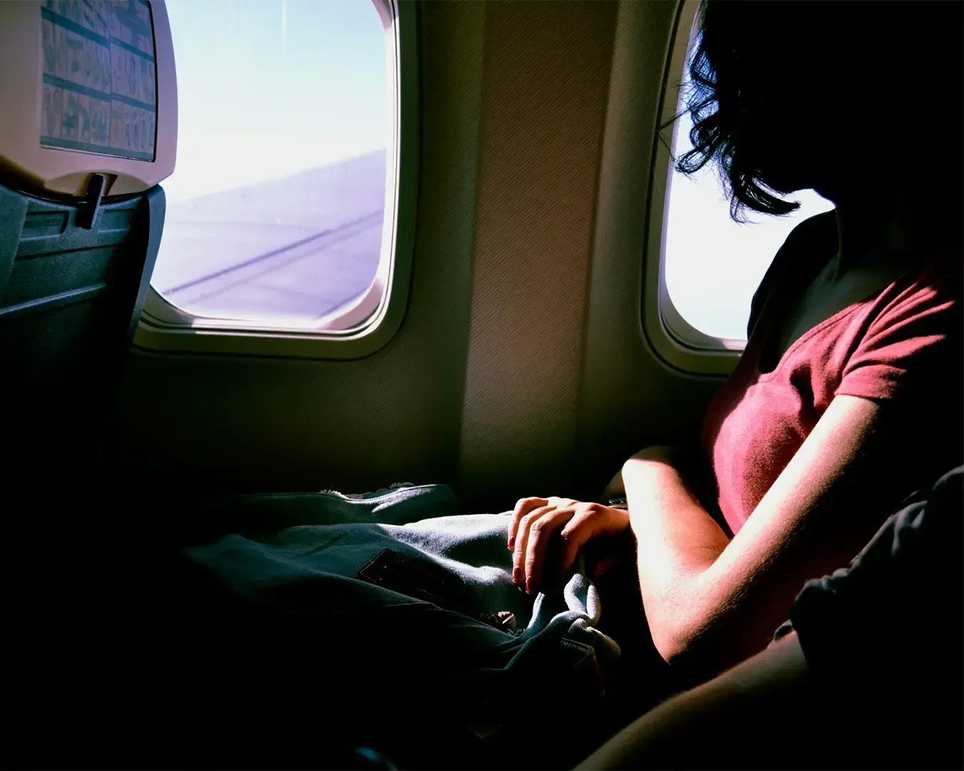 A woman sits beside an airplane window, gazing outside as soft daylight filters through the glass. 