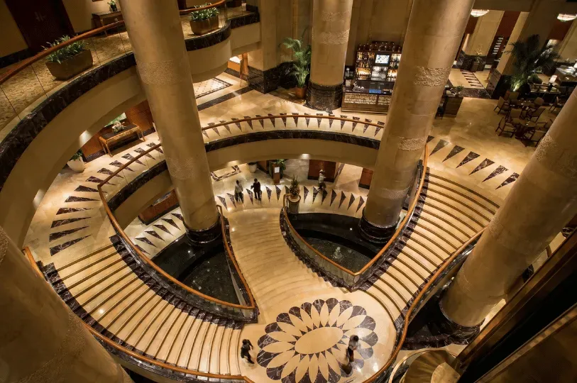 A high-angle view looking down into a grand luxury hotel lobby, featuring sweeping, multi-level curv