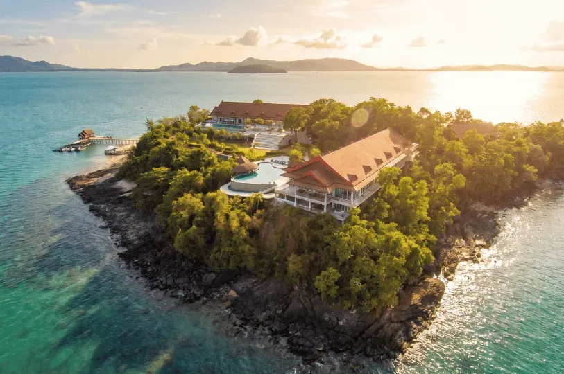 Aerial view of an exclusive private island resort at sunset, featuring large Thai-style luxury villa