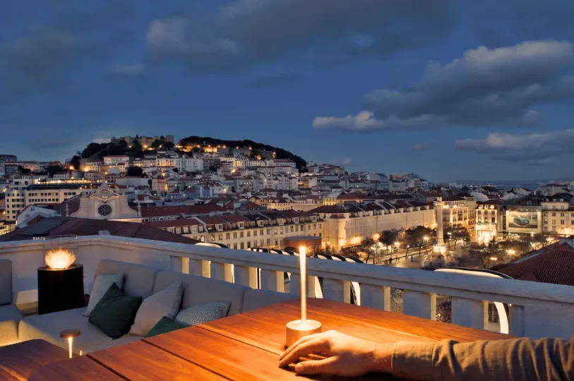 A first-person perspective of a solo diner's hand resting peacefully on a wooden table at a rooftop
