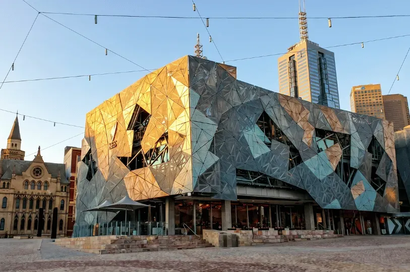 The geometric, shattered-glass style architecture of Federation Square in Melbourne glowing during g