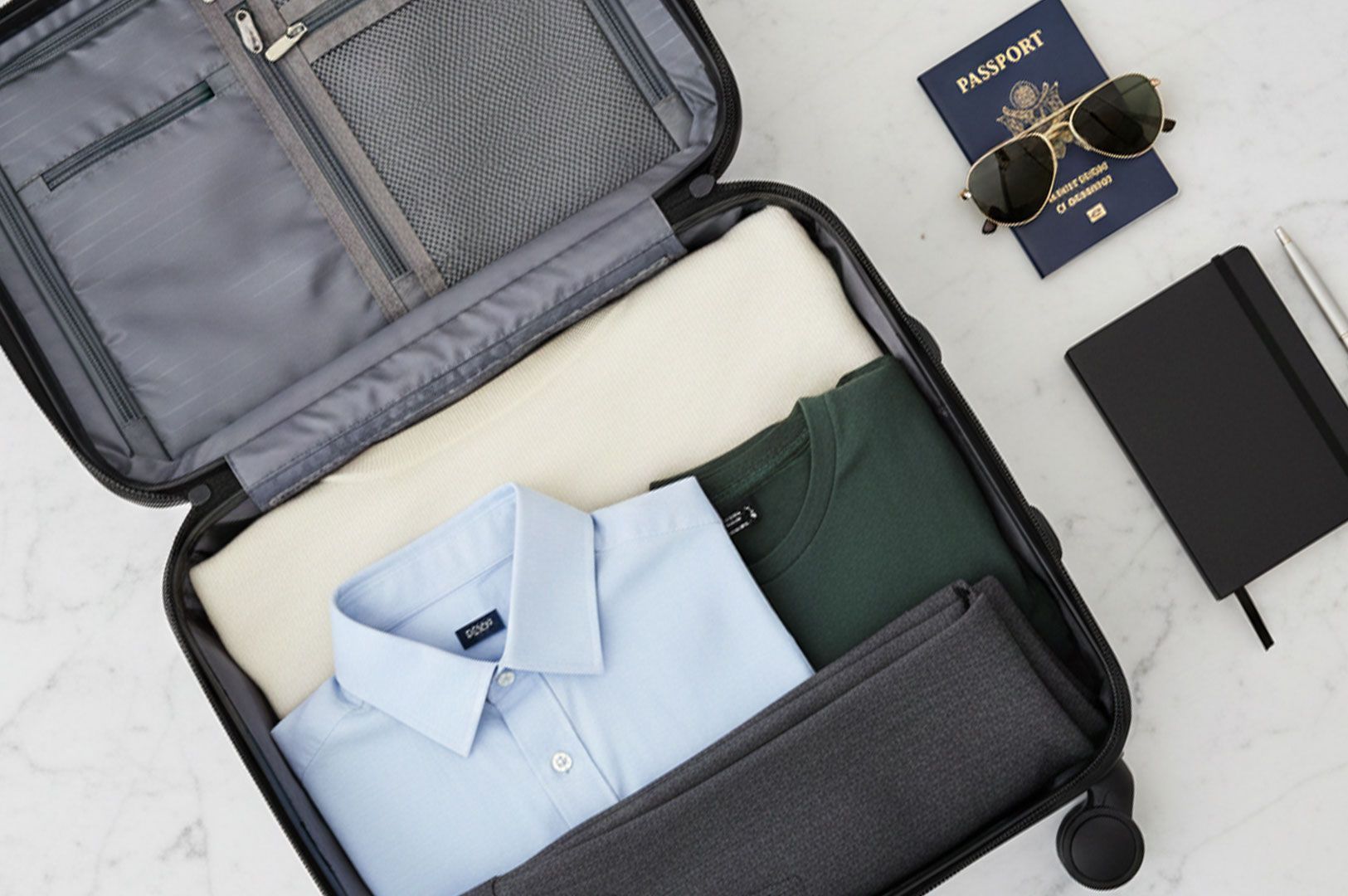 Top-down view of an open carry-on suitcase neatly packed with folded shirts and pants, placed next t