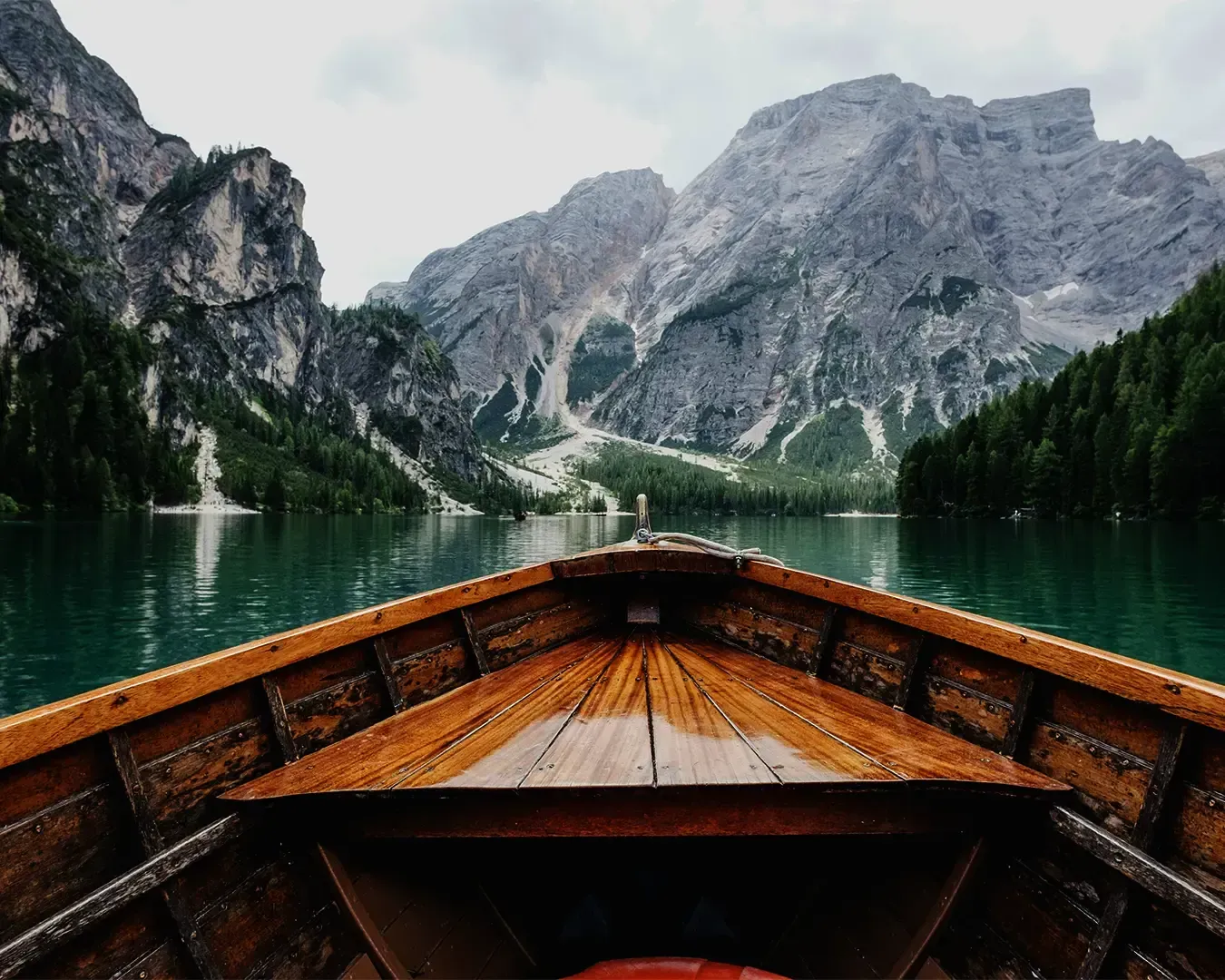 A peaceful scene from a boat floating on a lake surrounded by icy mountains. The still water reflects the snowy peaks, creating a dramatic and serene natural landscape.