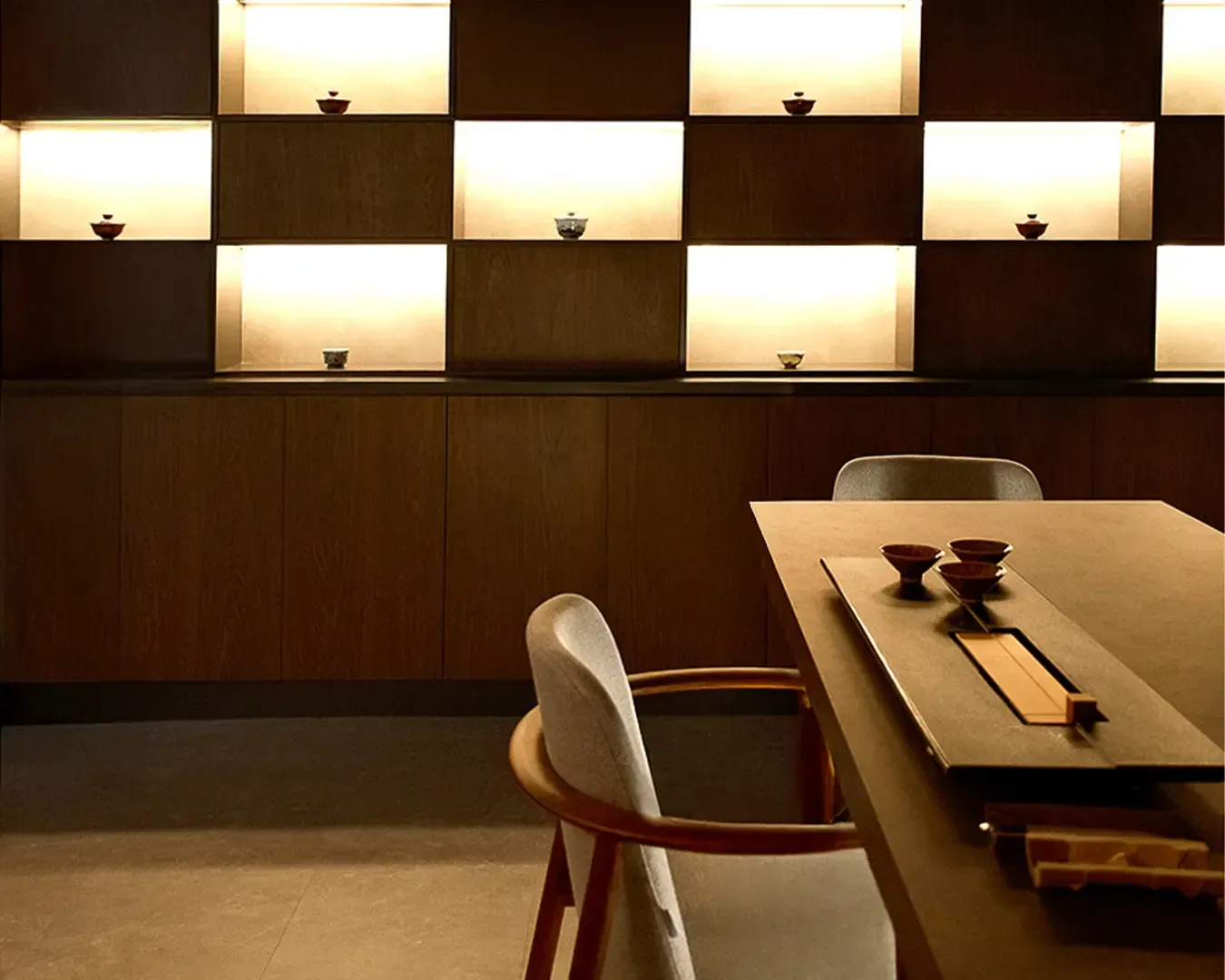 Warmly lit wooden shelving displays minimalist pottery, creating a serene and sophisticated atmosphere. A table set for tea sits elegantly nearby.