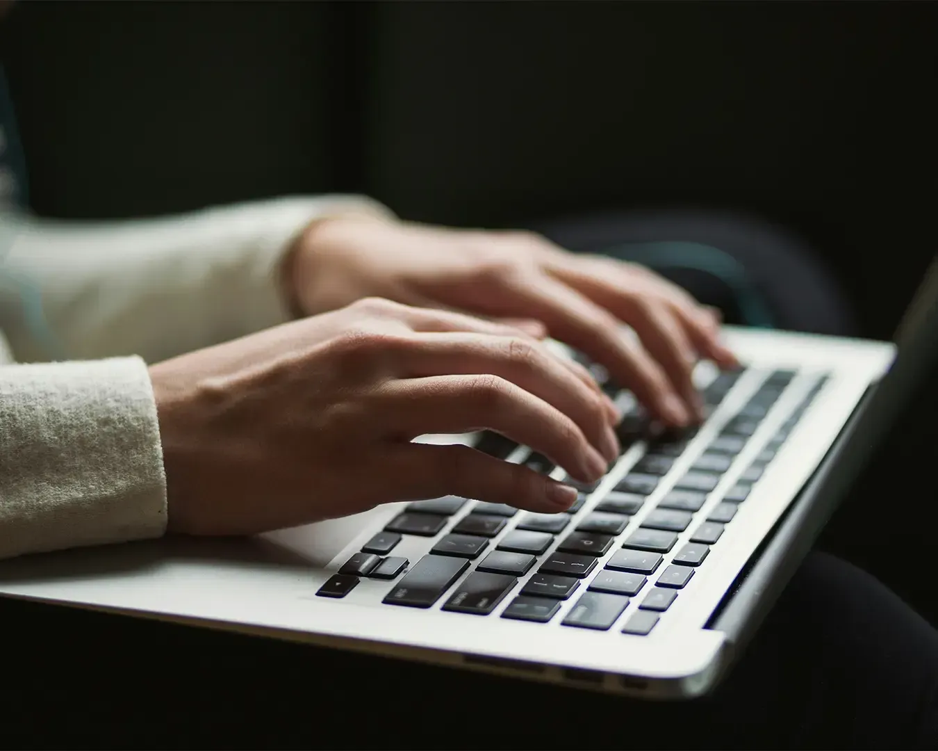 A close-up view of hands actively typing on a laptop keyboard, suggesting focus and productivity. The scene reflects a work environment, possibly involving writing, communication, or digital tasks.