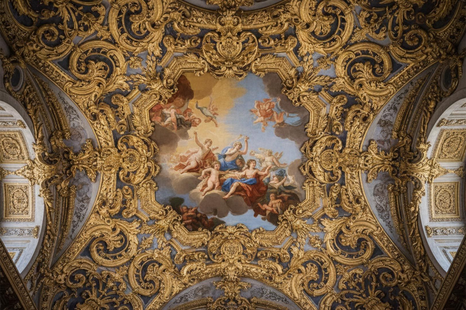 An intricate gold-leafed baroque ceiling featuring a central fresco painting of classical figures and cherubs in a blue sky.