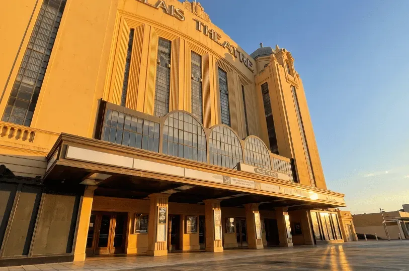 The grand, yellow Art Deco facade of Melbourne's historic Palais Theatre lit by the setting sun.