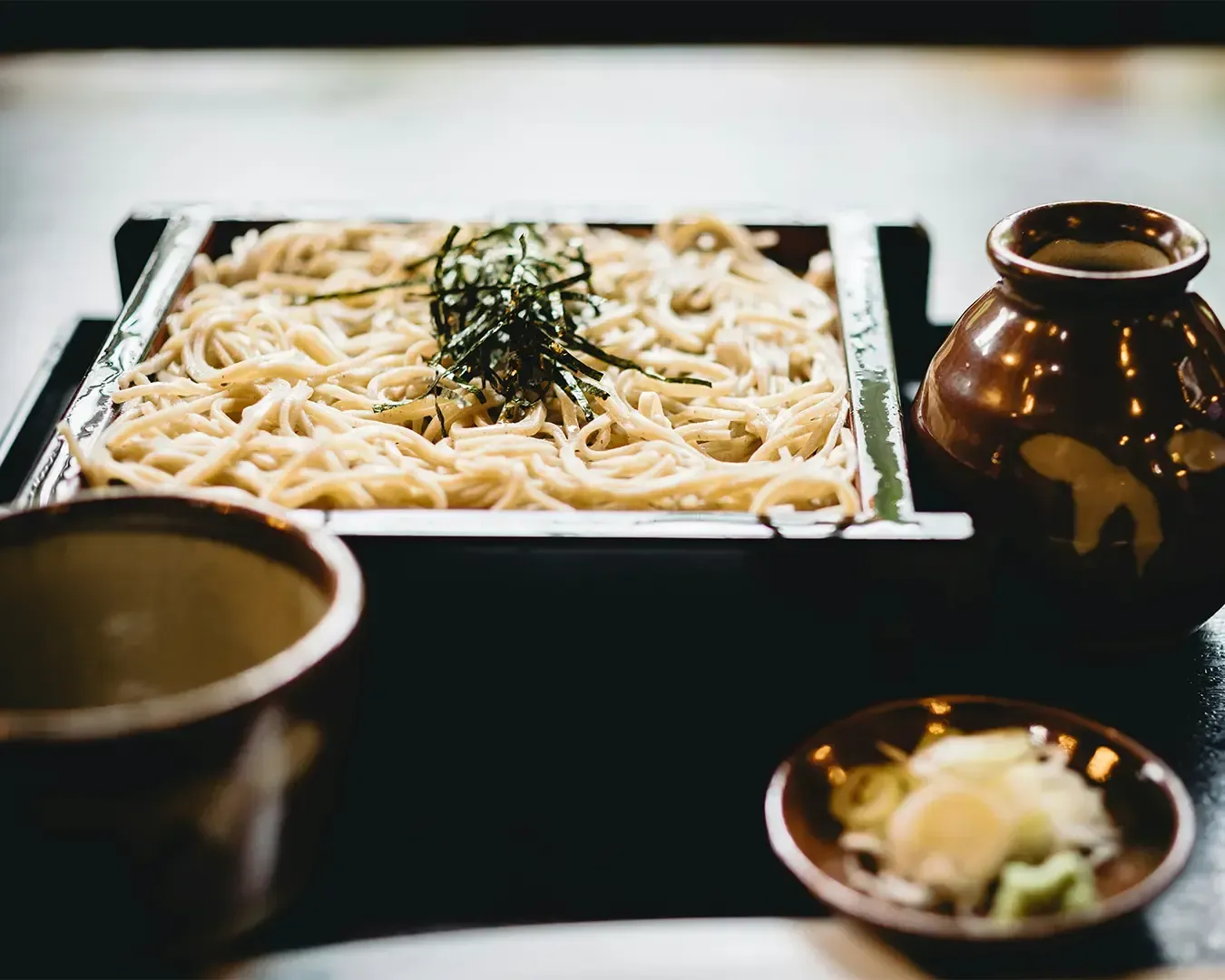 A neatly arranged set of soba noodles served with dipping sauce and side condiments, presented in a traditional style that highlights simplicity and balance.