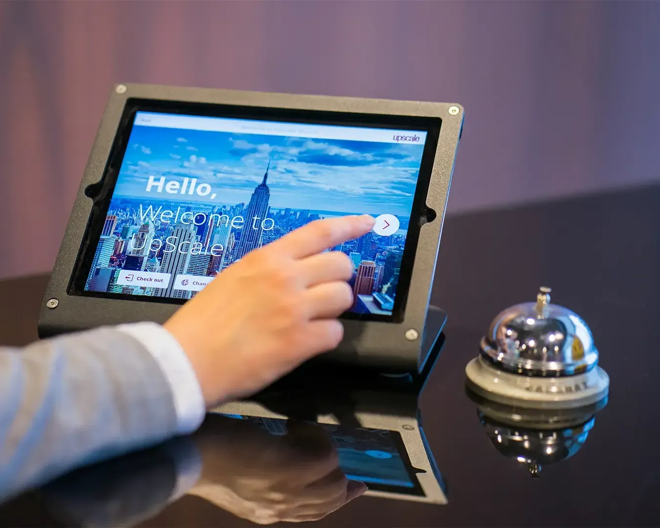 A receptionist interacting with a tablet device, likely managing bookings or checking in guests. The setting conveys a professional and modern front-desk environment, emphasising efficiency and customer service
