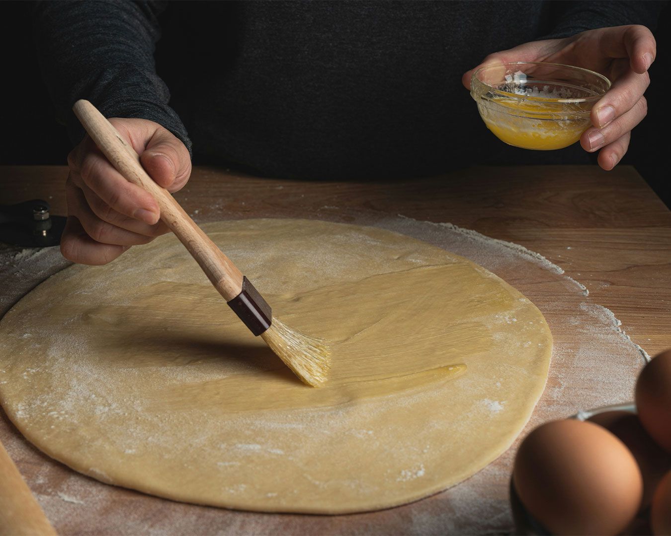 A close-up of a home chef carefully brushing melted butter onto fresh dough, highlighting the hands-on preparation and artisanal cooking process.
