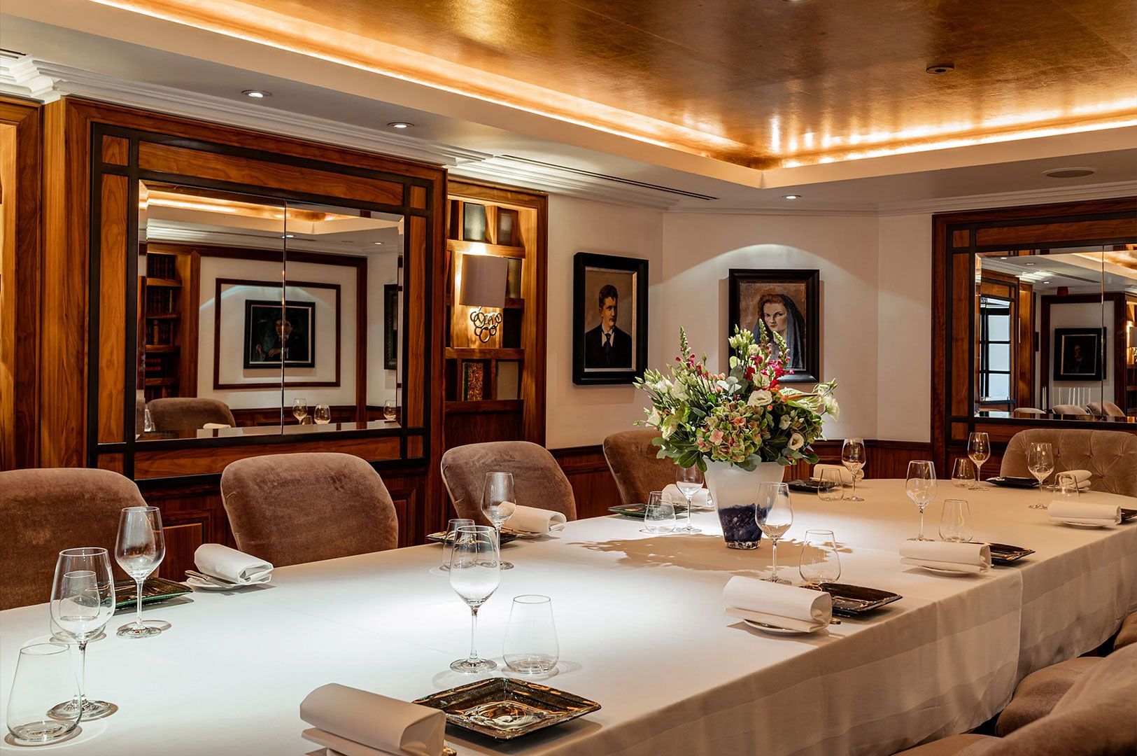 A luxurious, formal private dining room with a long white table set for a business meeting or exclusive dinner, featuring plush velvet chairs and wood-paneled walls with framed portraits.