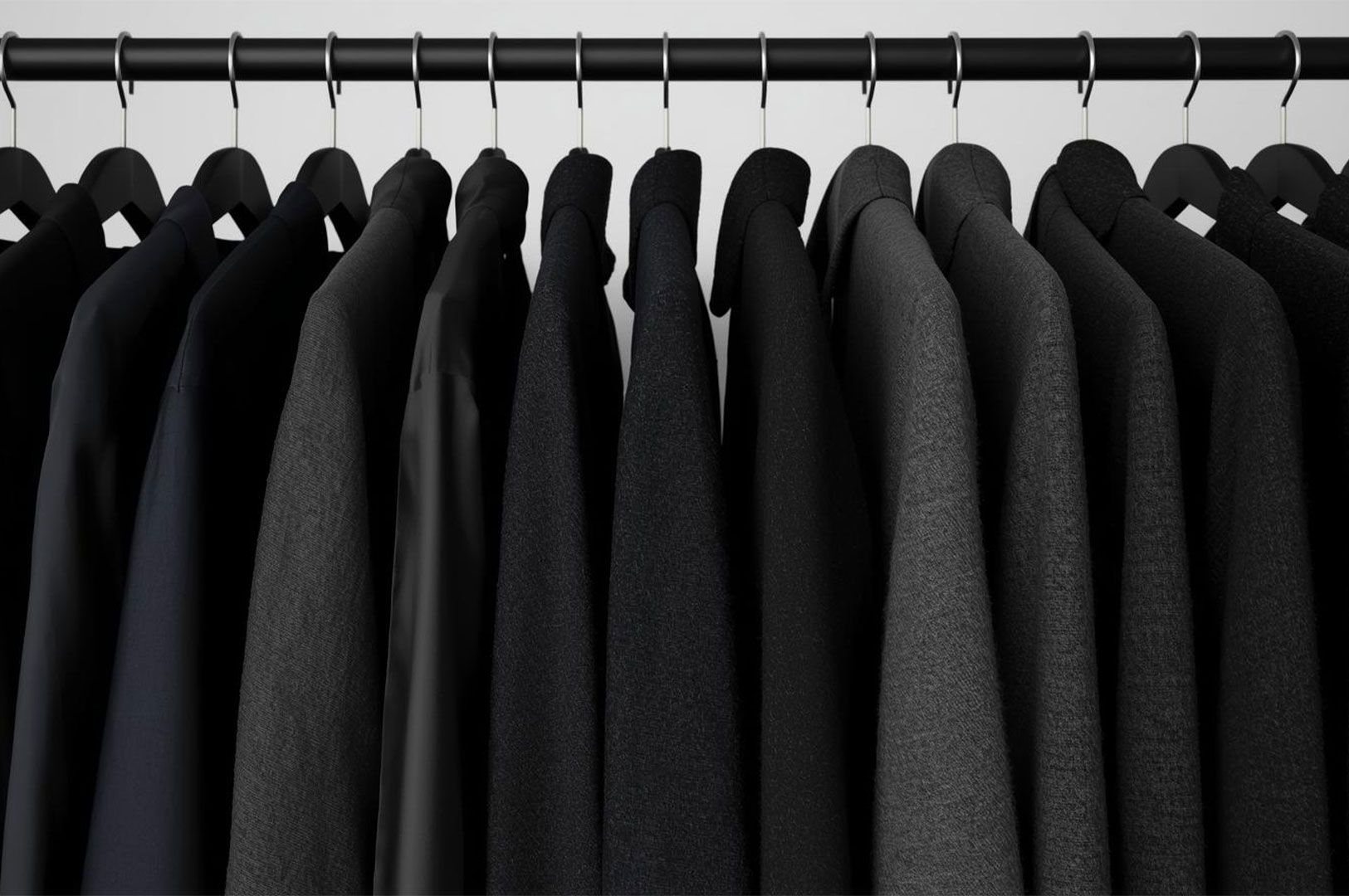 Close-up detail of a clothing rack filled with a monochrome collection of black and dark grey blazers, coats, and suit jackets hanging neatly in a row.