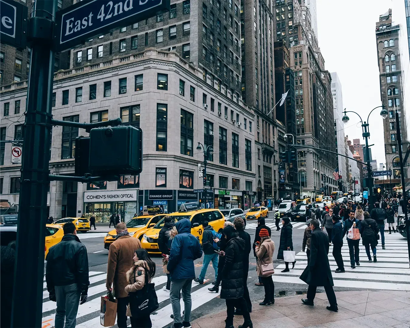 A busy New York City street scene with pedestrians crossing a zebra crossing while yellow taxis and tall skyscrapers frame the vibrant urban environment