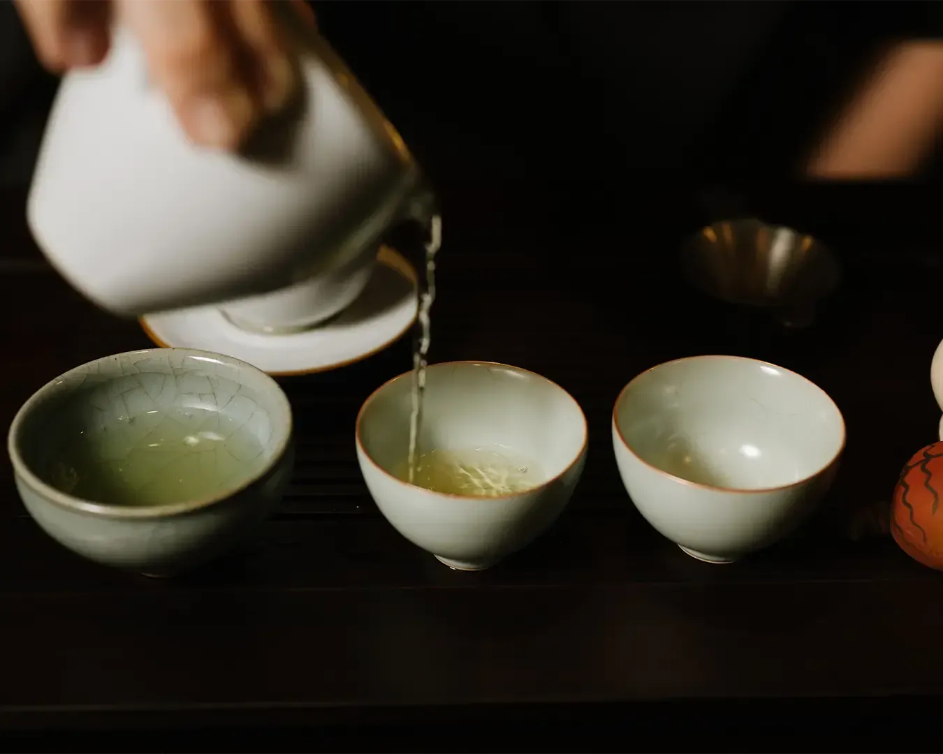 A hand gently pouring freshly brewed tea from a teapot into a small Chinese teacup, capturing the calm and mindful ritual of traditional tea preparation.