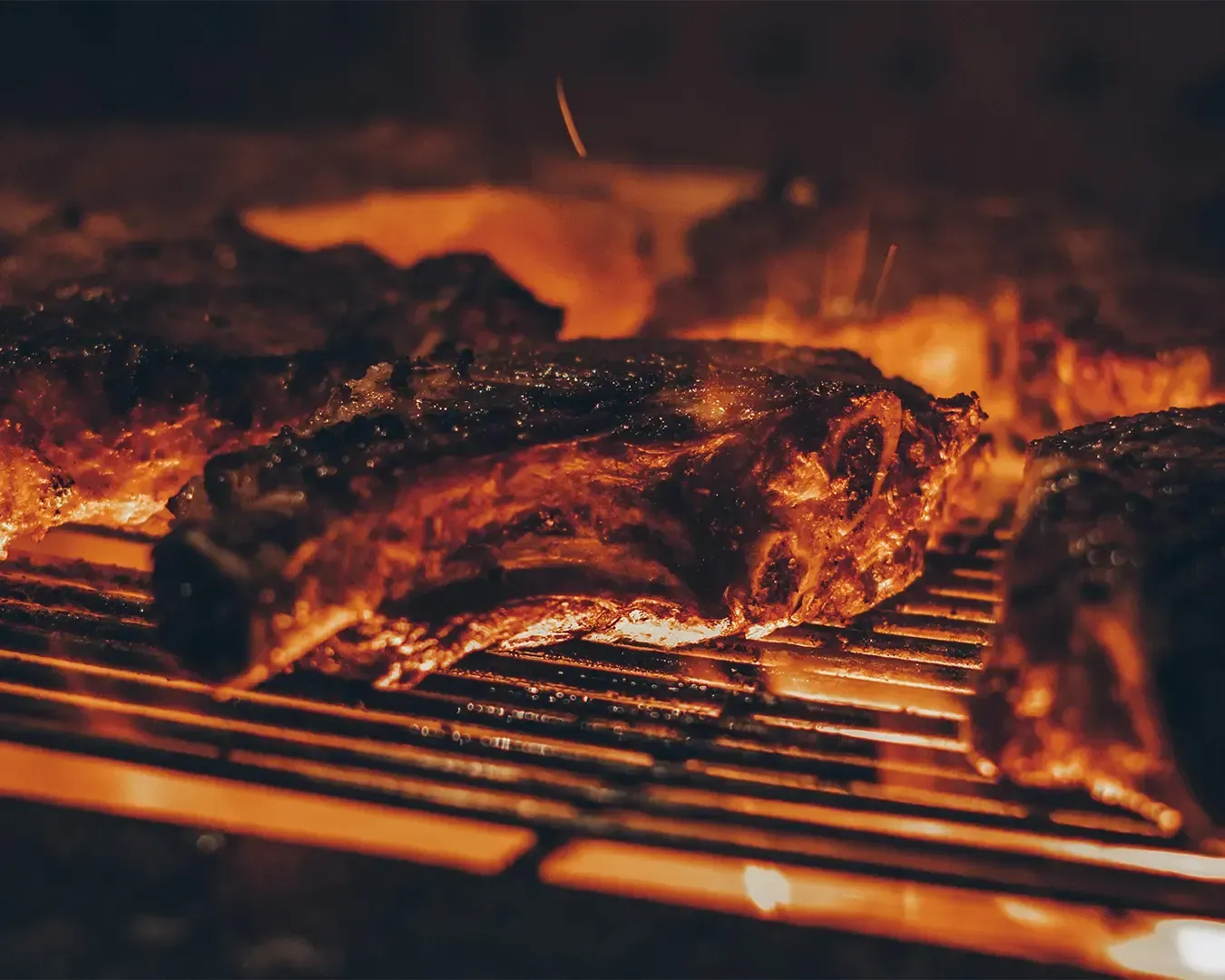 A piece of meats grilling over an open flame, with visible smoke and char marks, capturing the intensity of heat and the richness of the cooking process.