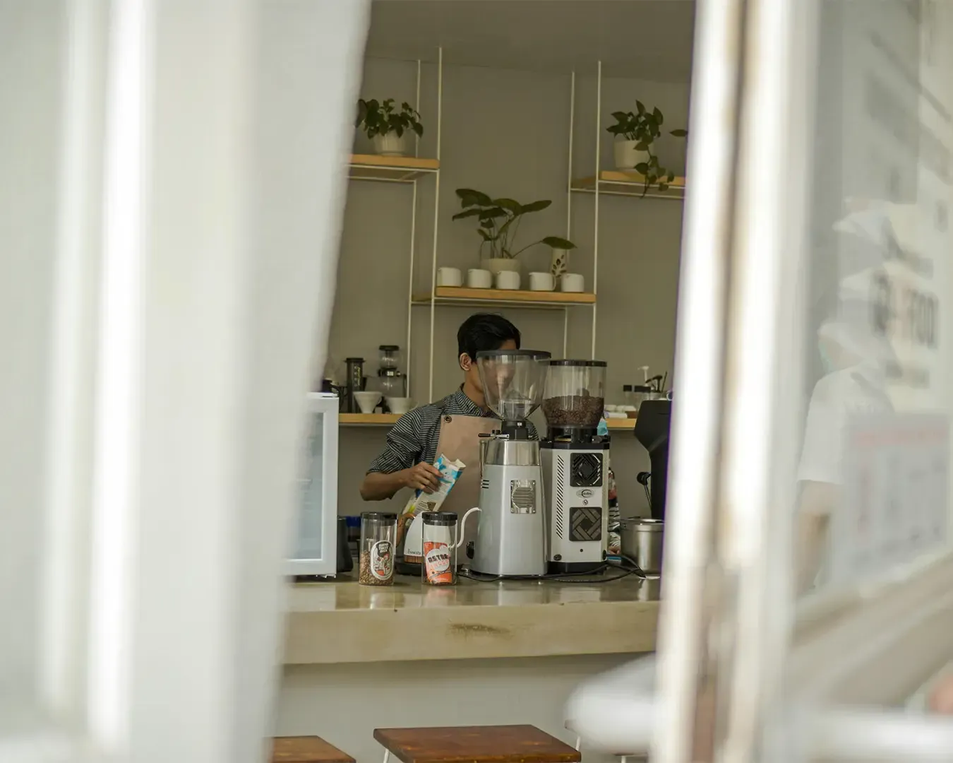 Professional barista standing behind a modern coffee counter, preparing coffee with espresso machines and café equipment in a warm café environment