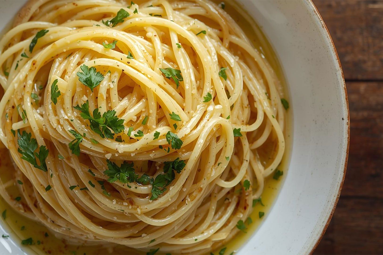 Close-up top view of a large bowl of spaghetti aglio e olio (garlic and oil) tossed with fresh parsley and sitting in a pool of clear sauce.