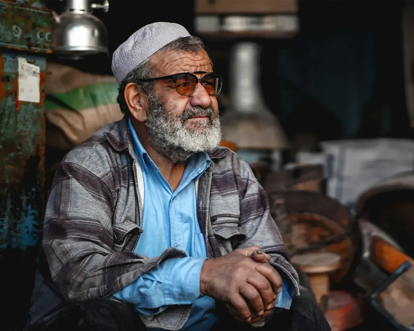 A Middle Eastern man wearing glasses sitting calmly and thoughtfully in a quiet space, captured in a candid moment that reflects a sense of reflection and stillness.