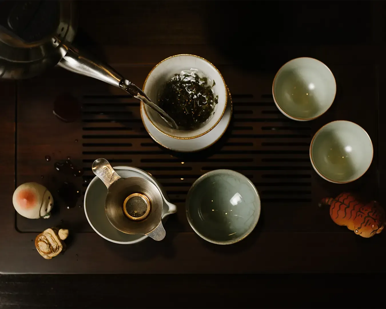 An overhead view of tea being slowly poured into a small teacup, showing the delicate colour of the tea and the careful precision of the tea ceremony.