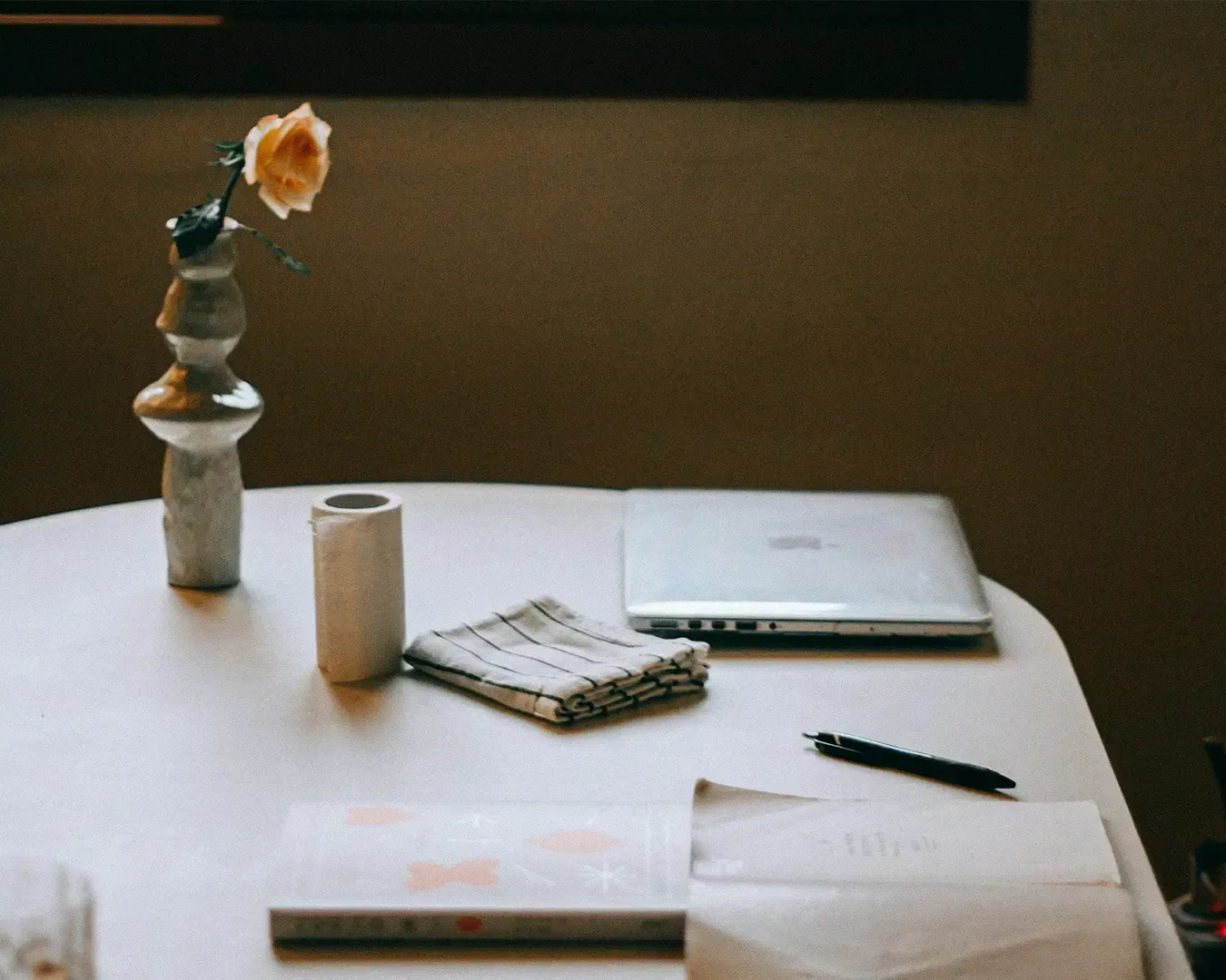A clean and minimal table setup featuring a laptop beside a small vase of flowers, combining a work environment with a touch of natural elegance.