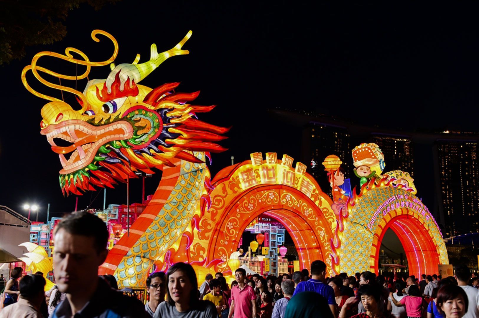 A massive, illuminated dragon lantern display at the River Hongbao festival in Singapore, with the Marina Bay Sands hotel visible in the night sky background.