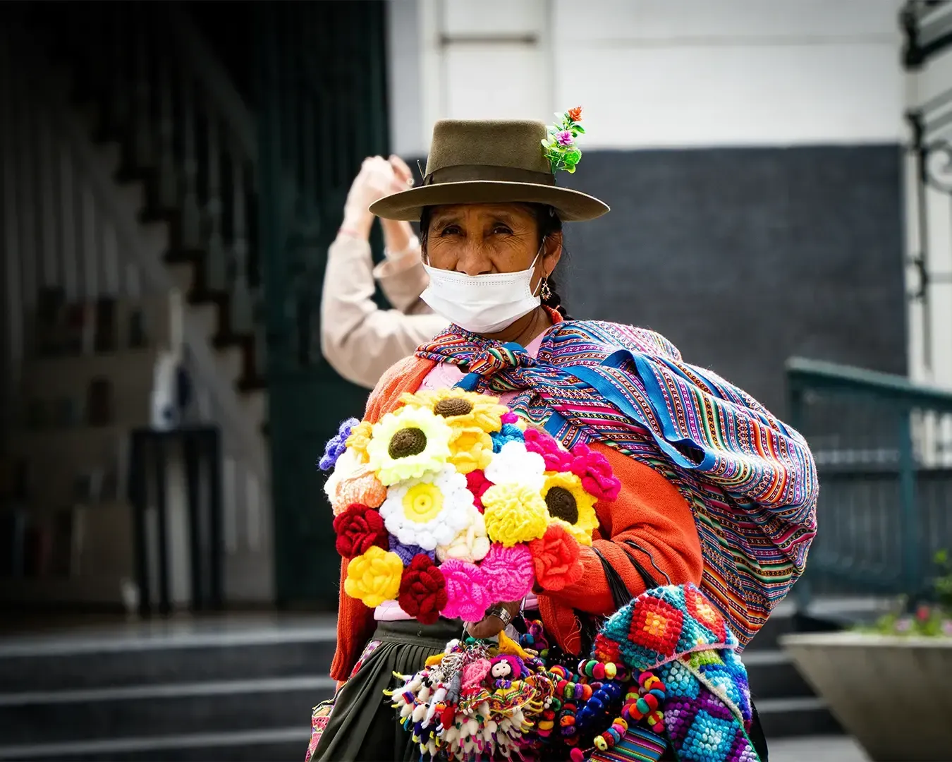 A Latin American street vendor with colourful handmade knitted flowers while walking at a small stall, adding warmth and craft culture to the lively street scene.