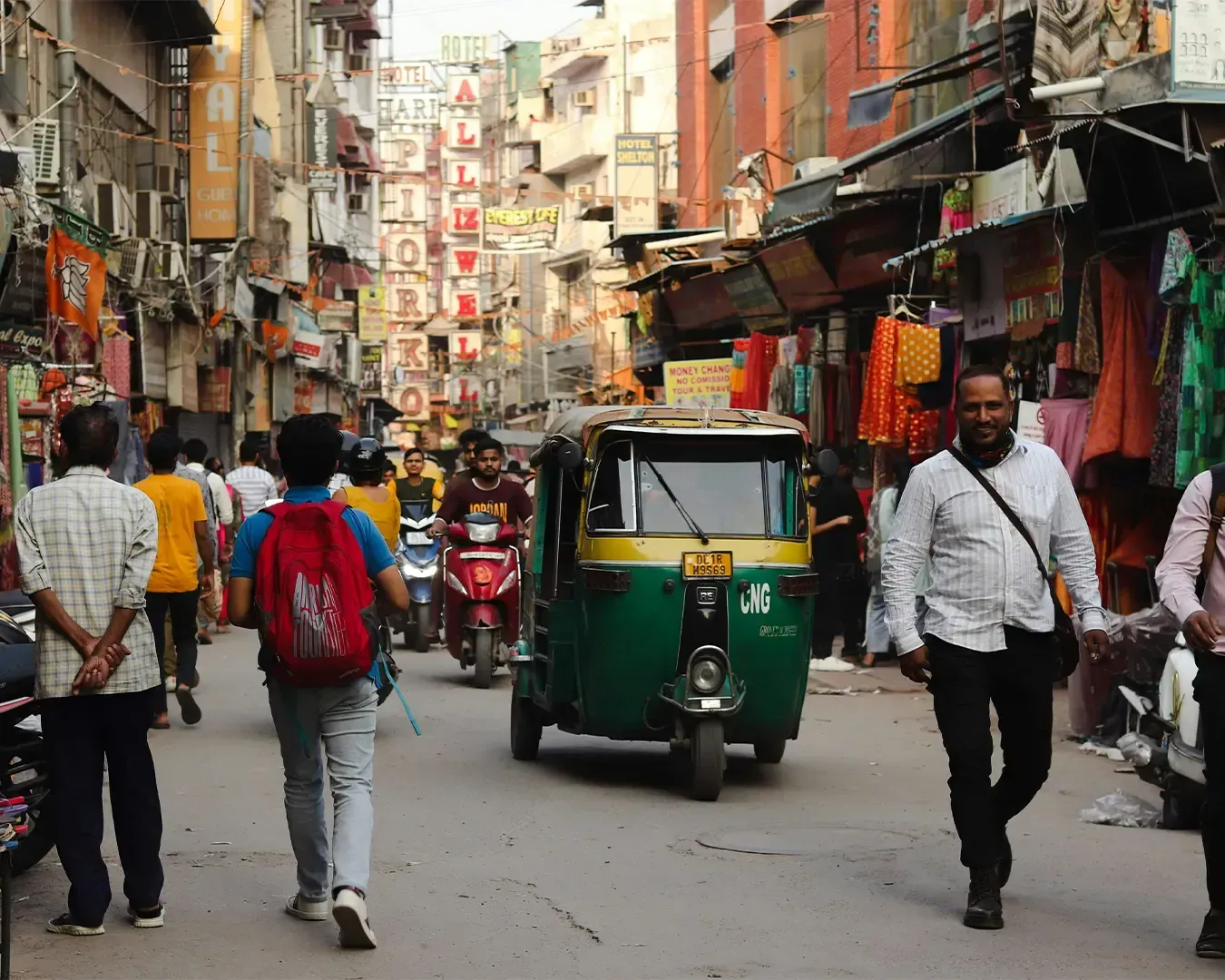 A vibrant Indian street filled with motorcycles weaving through traffic while pedestrians walk along busy roadside shops, capturing the energetic rhythm of daily city life.