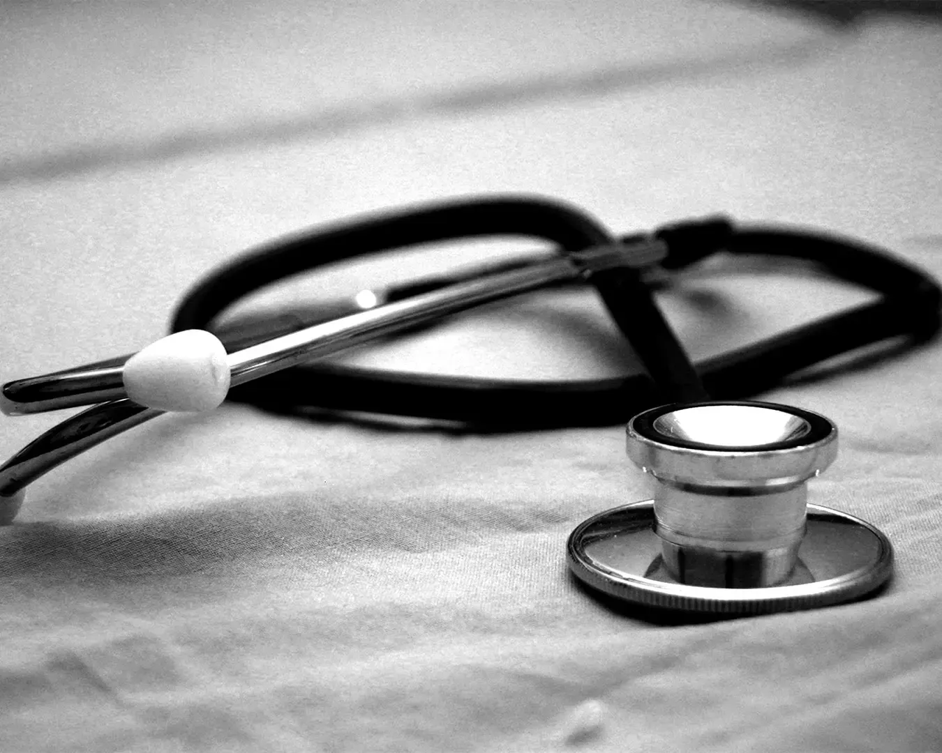 A close-up view of a doctor’s stethoscope resting against a medical coat or desk surface. The polished metal and tubing represent healthcare, professionalism, and the tools commonly used in medical examinations.