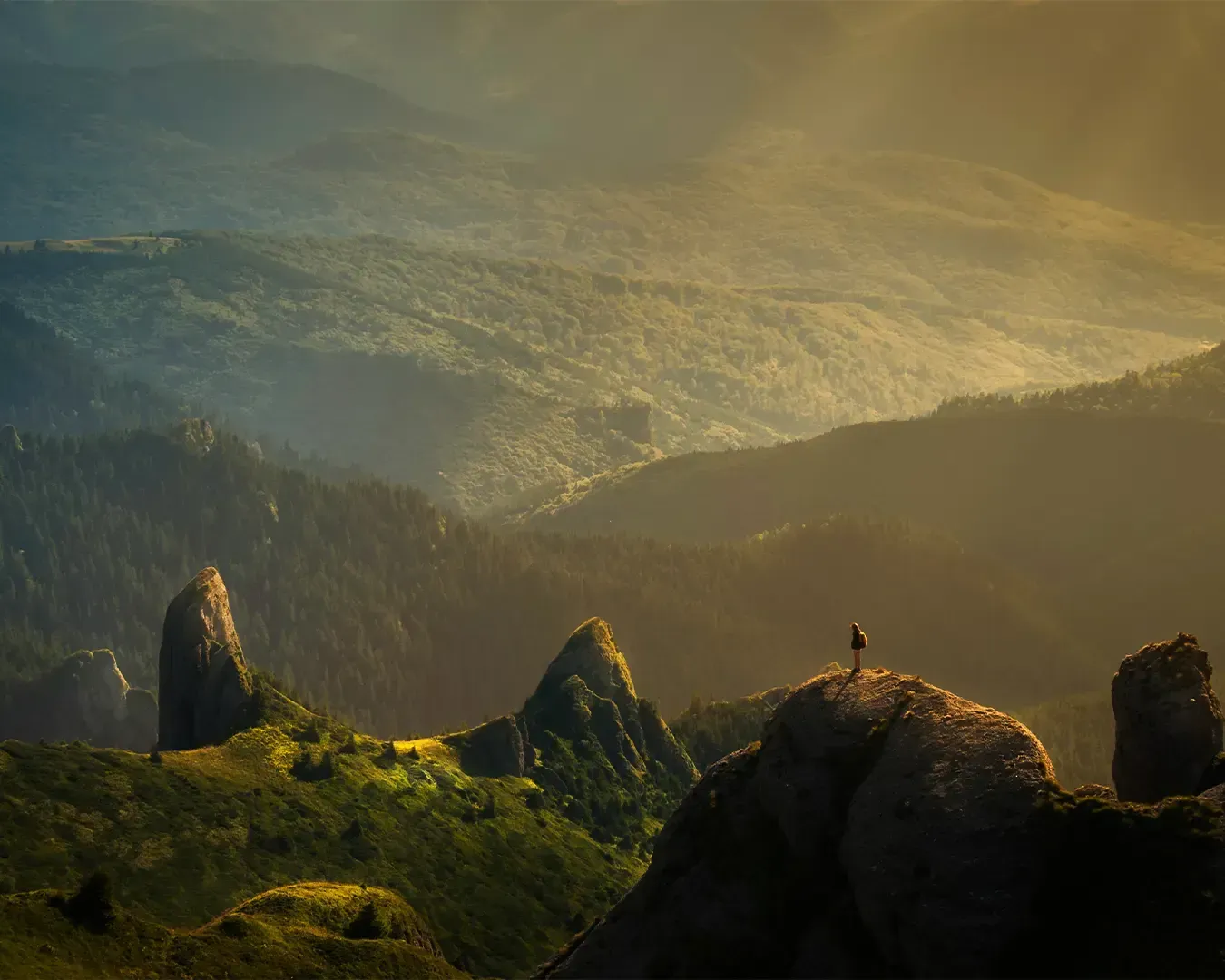 A bird’s-eye view of a woman standing at the peak of a mountain overlooking a vast sky and landscape. The scene conveys adventure, freedom, and achievement.