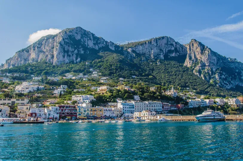 A vibrant Amalfi Coast town nestled at the base of towering, rugged mountains, with a ferry docked i