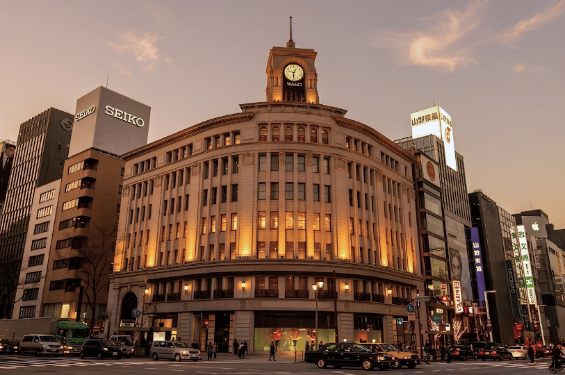 Warmly lit exterior view of the historic, curved Wako building in Ginza, Tokyo, at twilight. The clo