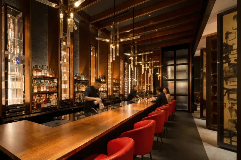 A sophisticated bar area in a Singapore fine-dining restaurant featuring a long live-edge wooden cou